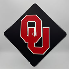 Load image into Gallery viewer, A black square graduation cap topper with a red OU (University of Oklahoma) logo in the center.